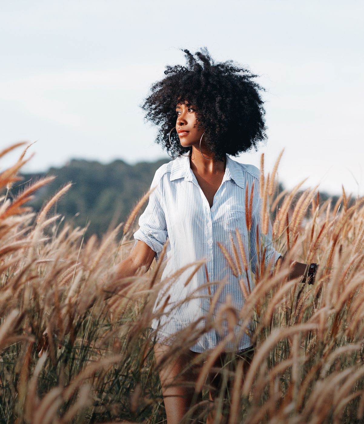 Woman in striped shirt among tall grasses.